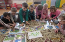 Skupione dzieci z grupy V segreguja na dywanie ilustracje dot. ekologii.