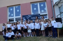 Dzieci stoja w grupie, machaja rekami, za ich plecami pracownicy przedszkola. W tle napis Zegnaj przedszkole.