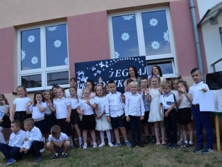 Dzieci stoja w grupie, machaja rekami, za ich plecami pracownicy przedszkola. W tle napis Zegnaj przedszkole.