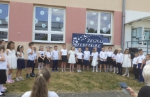 Dzieci ustawione w polkolu spiewaja piosenke, w tle napis Zegnaj przedszkole.