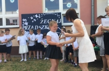 Pani dyrektor oraz przedstawicielka rodzicow wreczaja dziewczynce dyplom i ksiazke.