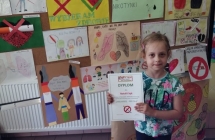 Dziewczynka na tle wystawy prac plastycznych z dyplomem w rekach