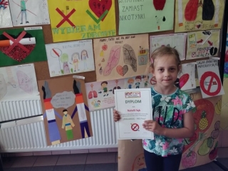 Dziewczynka na tle wystawy prac plastycznych z dyplomem w rekach