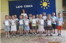 Usmiechniete dzieci z gr. V z p. dyrektor pozuja na tle napisu - Lato czeka.