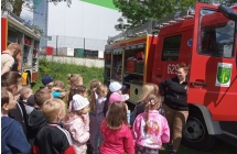 Dzieci zgromadzone przed bojowym samochodem strazackim sluchaja opowiadania pani strazak