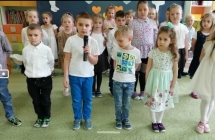 dzieci ustawione w rzedach, chlopiec w bialej koszuli mowi wiersz przez mikrofon