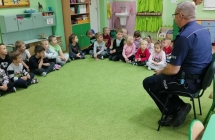 Dzieci siedzace w kole sluchaja opowiadania policjanta