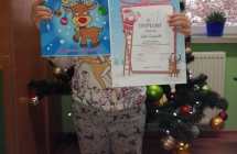 Dziewczynka z dyplomem na tle choinki.