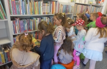 Dzieci z gr. VII wybieraja ksiazki z regalu liaratury dzieciecej.