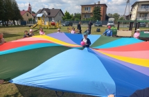 Wesołe dzieci z gr VII podczas zabaw z dużą chustą w ogrodzie.