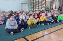 Dzieci siedzące na podłodze i skupione na wydarzeniu szkolnym 