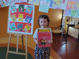 Uśmiechnięta dziewczynka trzymająca dyplom. W tle obrazki