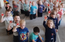 Dzieci siedzące na kształcie serca pokazują wycięte serca umieszczone na dłoni 