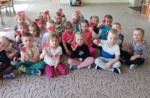 Uczniowie przedszkola siedzący na dywanie i pokazujący serduszka na dłoni 