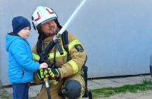 Chlopiec ze strazakiem leje wode wezem gasniczym.