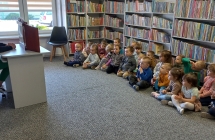 Siedzace na dywanie dzieci sluchaja basni czytanej przez p. bibliotekarke.