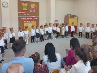 Dzieci z gr. I w opaskach misiach stoja przed rodzicami.