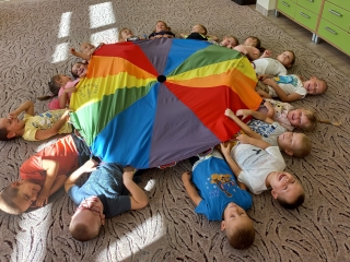 Rozbawione dzieci na dywanie z kolorowa chusta animacyjna.