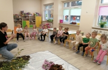 Pani pedagog opowiada dzieciom siedzacym na krzeselkach w kregu.