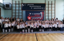 Spolecznosc przedszkolna w sali gimnastyczne j przed odspiewaniem hymnu.