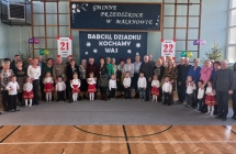 Grupowe zdjecie dziadkow i wnuczat z gr. III  na tle napisu w sali gimnastycznej.
