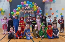 Usmiechniete dzieci z gr. III w strojach balowych na tle kolorowych balonow.