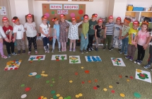 Rozesmiane dzieci z gr. VI przed obrazami ulozonymi z kol na dywanie.