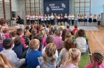 Dzieci spiewaja piosenke trzymajac papierowe kwiaty w reku.