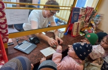 Dzieci przyklejaja znaczek z pomoca pracownicy poczty.