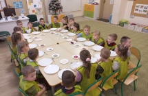 Pieciolatki w fartuszkach przy stolikach.
