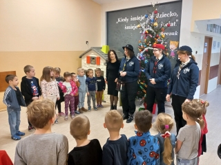 Harcerki ze swiatelkiem betlejemskim i p. dyrektor na tle choinki
