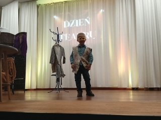 11. Chlopiec w okularach i surducie stoi na scenie. Inscenizacja wiersza Okulary. (2)