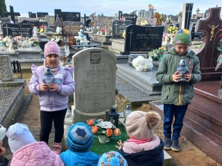 Przedszkolaki ze zniczami przy grobie dzieci.