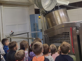 Dzieci  z grupy VII ogladaja proces przekladania gotowego ciasta chlebowego do krajalnicy.