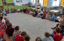 Pani pielegniarka wita szesciolatki siedzace w kole na dywanie.