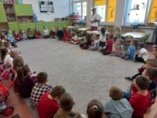 Pani pielegniarka wita szesciolatki siedzace w kole na dywanie.