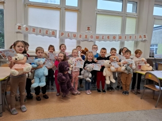 Dzien Pluszowego Misia w grupie dzieci piecioletnich. Dzieci stoja zew swoimi misiami, prezentuja otrzymane dyplomy.
