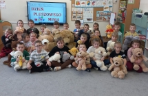 Dzieci z gr. IX ze swoimi misiami na tle napisu Dzien Pluszowego Misia.