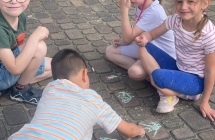Dzieci z grupy Wiewioreczki rysuja kreda obrazki na chodniku.