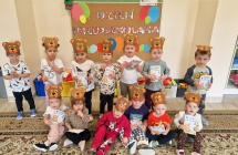 Zdjecie grupowe na tle napisu Dzien przedszkolaka z dyplomami i opaskami niedzwiadkow.